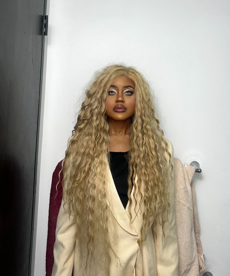 Samantha Samaka in a beige blazer, long blonde curls